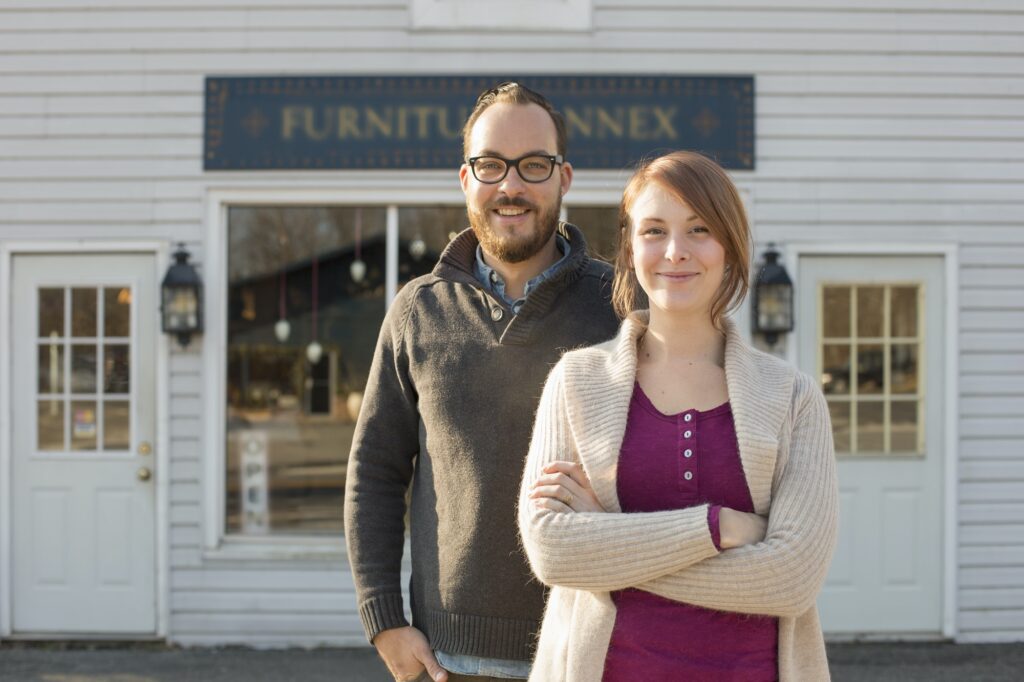 A man and woman standing outside a storefront on a street. A couple running an antique shop.