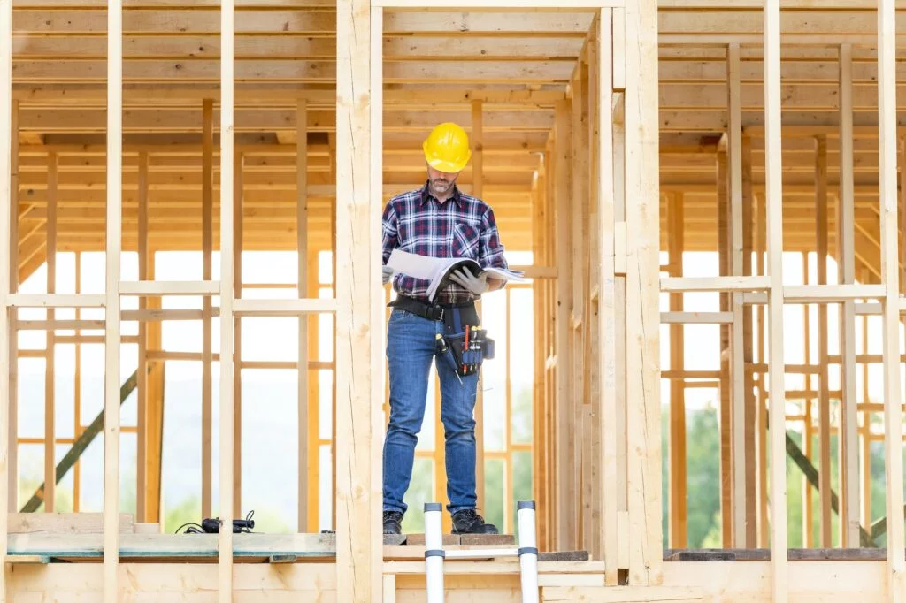 Builder reading blueprints plan of wood construction frame house